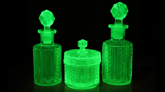 Art deco molded green uranium glass lit by UV light on a table. The uranium glows green with fluorescence.